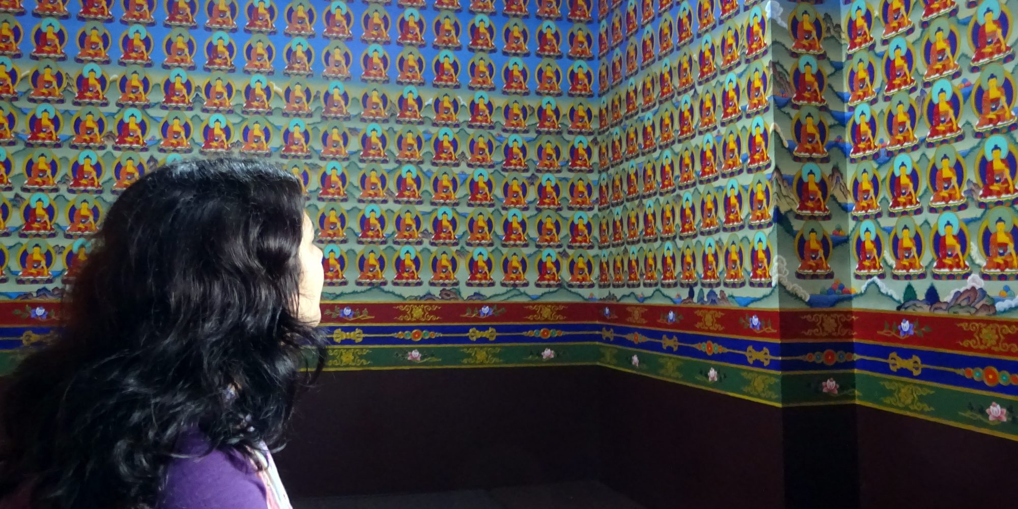 black haired woman looking up at walls covered in buddha icons