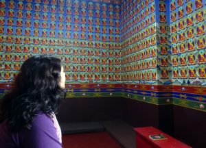 black haired woman looking up at walls covered in buddha icons