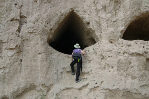 woman climbing and peering into hole in side of cliff