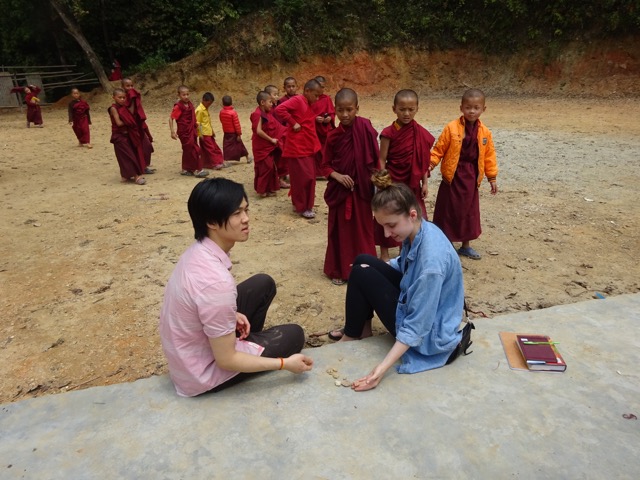 man and woman sitting being approached by line of young monks