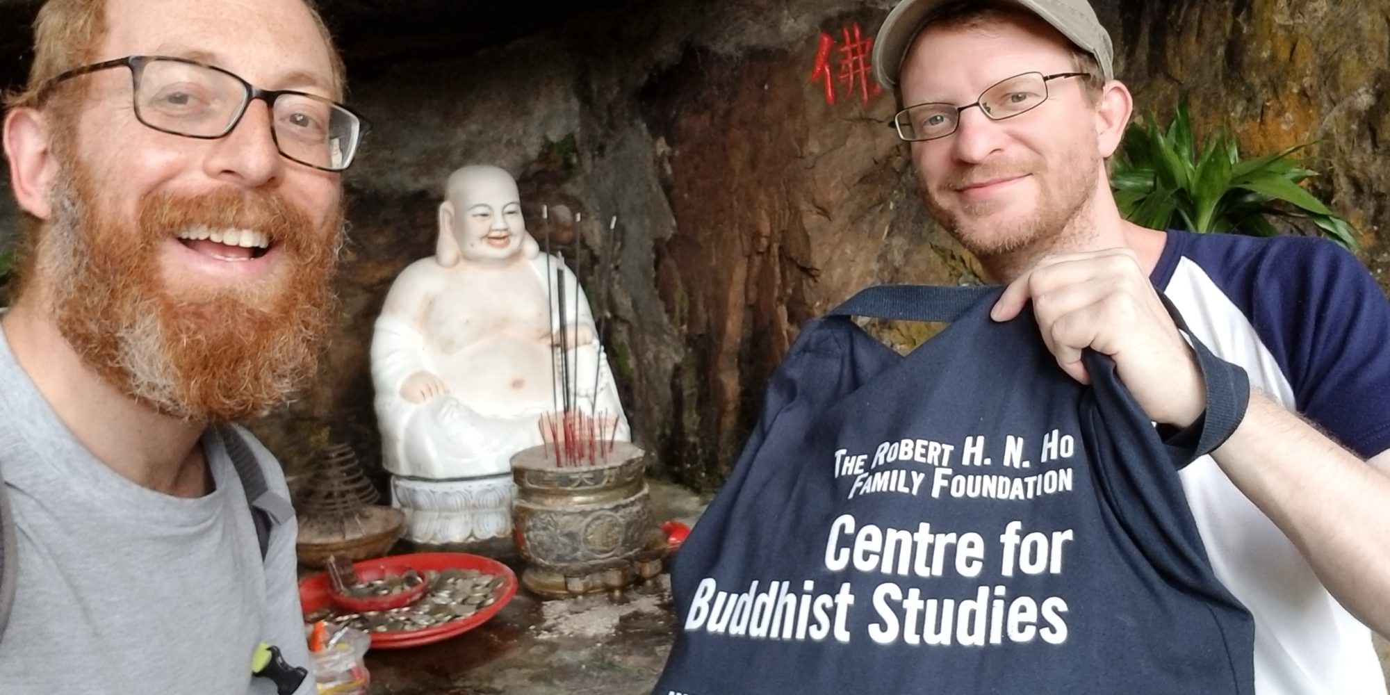 selfie of two men with glasses posing in front of buddha statue