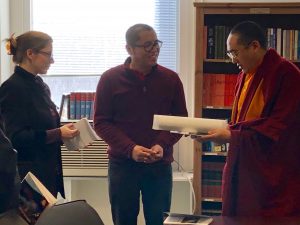 two academics in discussion with monk holding text