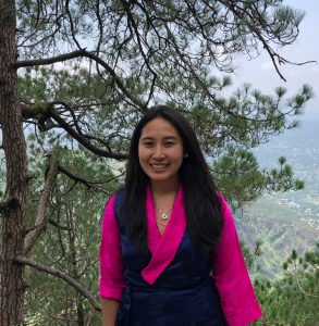 young woman in pink and blue robe smiling atop a mountain