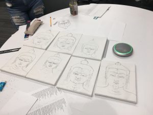 a collection of student-made buddha drawings following template laid out on table