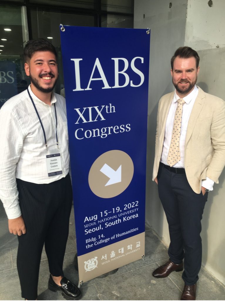 Ian and Austin smiling next to the banner for the 19th Congress of the International Association of Buddhist Studies.